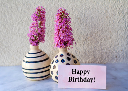 Happy Birthday card with purple flowers in vase and white wall backgroundの写真素材