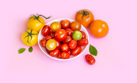 Colorful cherry tomatoes in a white bowl on a pink background.の写真素材