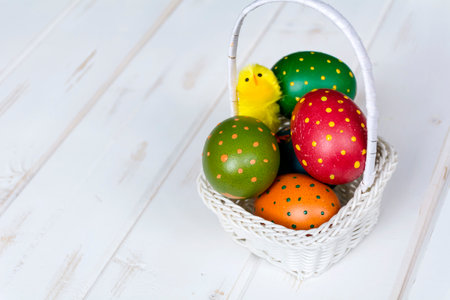 Colorful easter eggs in a basket on a white wooden backgroundの写真素材