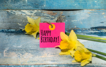 Happy birthday card with yellow daffodils on a blue wooden backgroundの写真素材
