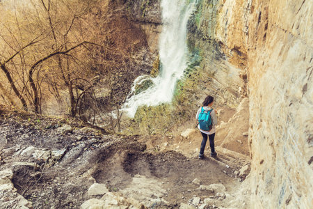 Young woman traveler with backpack hiking in the mountains and looking at waterfall.の写真素材