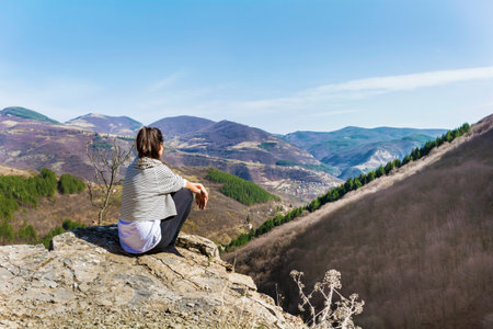 Young woman sitting on top of a mountain and looking at the valleyの写真素材