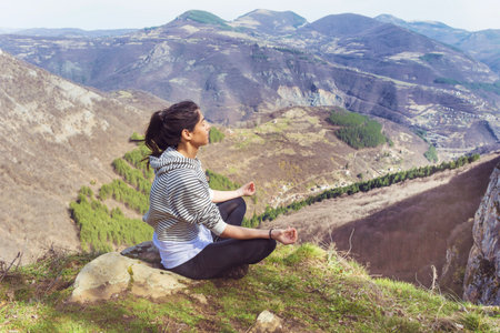 Young woman practicing yoga on top of a mountain in the mountains.の写真素材