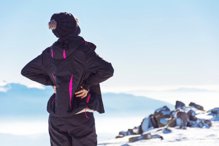 Back view of young woman in black sportswear standing on top of mountainの写真素材