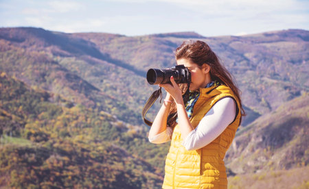 Young woman taking photo with camera in autumn mountains. Travel and adventure concept.の写真素材