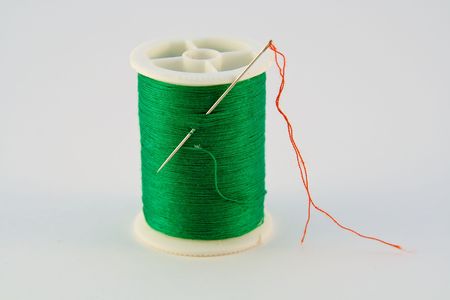 A Green Spool of Thread armed with a needle left over from a red thread repair