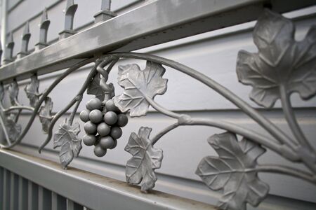 oblique view of grey wroght iron gate with a design og grapes and grape leavesの写真素材