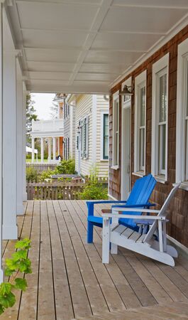 Blue and white adirondack chairs on a the wood porch of a brown shake home