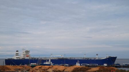 Large blue freighter ship having lumber loaded with a cloudy skyの写真素材