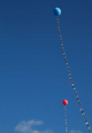 Two  helium balloons, one red and one blue, held in place by a flagged line against a blue skyの写真素材