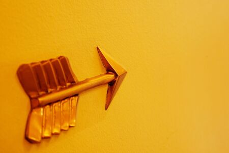 Soft focus tail to sharp point of brass arrow on yellow wallの写真素材