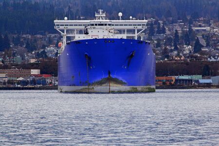 Huge blue freighter bow pointed toward viewer with port town in backgroundの写真素材