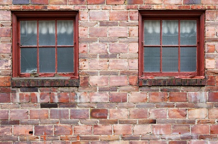 Multi red shaded ugly old brick wall with twon weathered wood windowsの写真素材