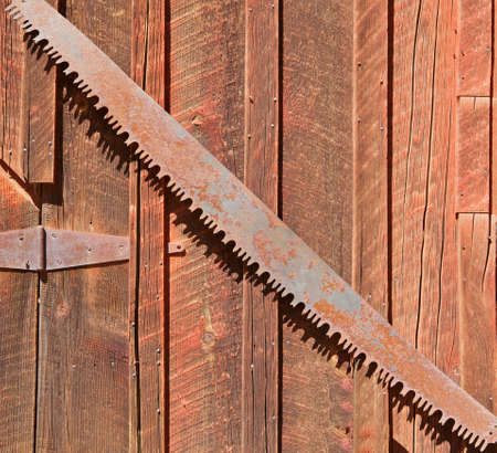Old rusted lumberjack's saw on an old weathered brown barn wallの写真素材