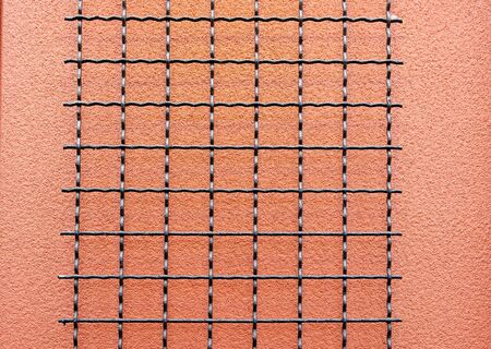 Black wire grid against a salmon stucco wallの写真素材