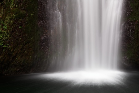 Frothy misty bottom of a waterfall falling into a dark pool of waterの写真素材