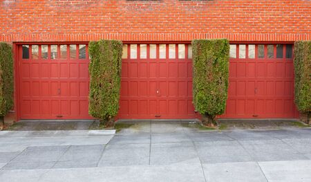 Three Red Garages on a brick wall separaged by evergreen bushesの写真素材