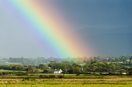 Rainbow appearing to end over a houseの写真素材