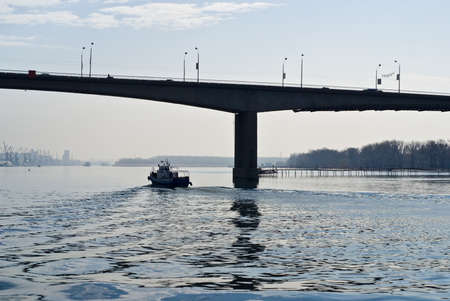 A small boat floating on the river under the bridgeの写真素材