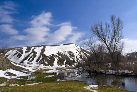 Small meadow by the river, surrounded by low mountains with snow patchesの写真素材