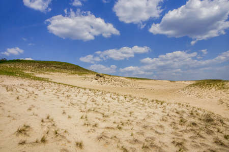 a small stretch of sandy desert under a blue sky with cloudsの写真素材