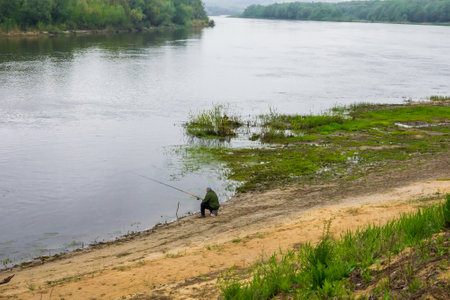 a man with a fishing rod on the bank of a big riverの写真素材