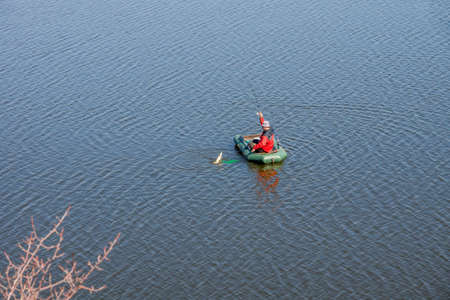 a man in a rubber boat pulls a pike out of the waterの写真素材