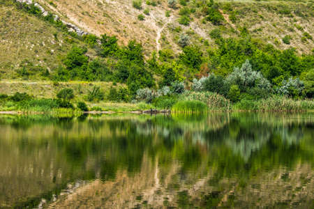 The Seversky Donets River near the town of Belaya Kalitva. Distorted reflections of a picturesque steep coast with a rocky exit in the waterの写真素材