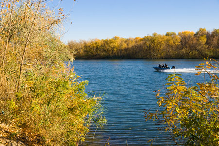 The Don River near the village of Romanvskaya Rostov Region, Russia. The blue water of the river is framed by yellow wooded banks. A boat with people is moving fast along the river. It's a cloudless and sunny dayの写真素材