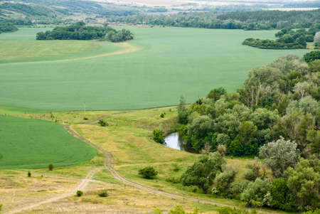 View of the picturesque valley of the Kalitva river from a high point. Green cultivated fields surrounded by wild forestの写真素材