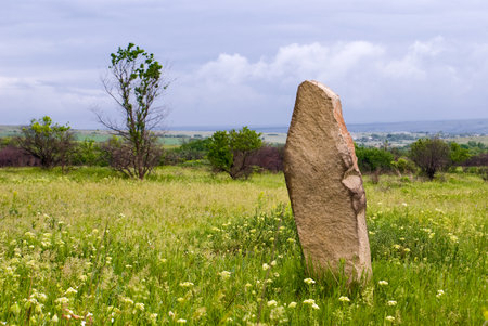 Old sandstone boundary stone among the green steppe on a cloudy summer dayの写真素材