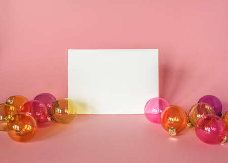 Mock up with invitation card on light pink background with christmas ornaments. Greeting card and colorfull translucent glass Christmas baublesの写真素材