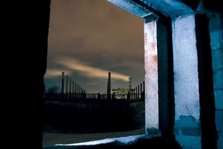 Industrial smoke from a pipe in a night through an empty industrial abandoned building window.の写真素材