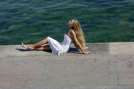 blonde in white near sea sitting on a pierの写真素材