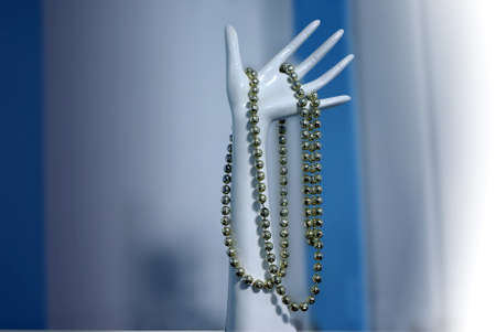 white plastic female hand with metallic necklace over blue