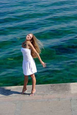 blonde in white near sea standing on a pier with open hand emotionally.の写真素材