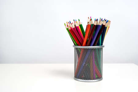 Various color pencils in silver office cup on white table and white background. School. Kids.