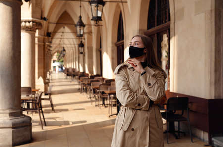 Woman wearing trendy fashion outfit during quarantine of coronavirus outbreak. Model dressed protective stylish handmade face mask. Tourist walkin on empty street. Beautiful blonde woman with fashion protective mask. Architecture background. Streetの写真素材