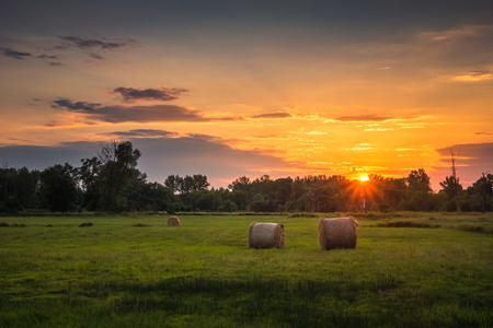 Sunset over the meadow and bales of strawの写真素材