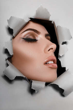 Close-up portrait of girl with evening makeup, closed eyes, opened relaxed sensual full lips from a ripped paper backgroundの写真素材