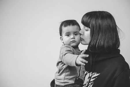 Black and white portrait of young mother kissing her son, toddler with serious sad expression, lots of place for textの写真素材
