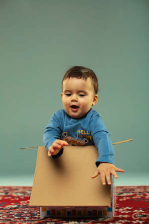 Laughing happy male toddler trying to get out of carton box on the colorful carpet isolated in studioの写真素材