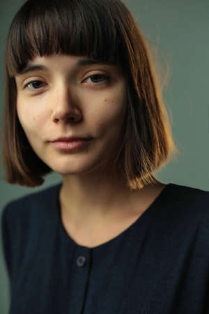 Close up portrait of attractive young woman brunette without make up with short dark hair and straight bang is looking at camera isolatedの写真素材