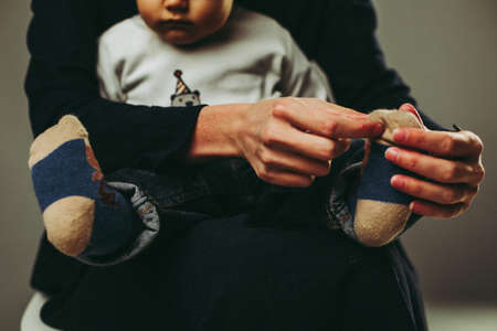 Hands of mother adjusting sock of her toddler sitting on lapsの写真素材