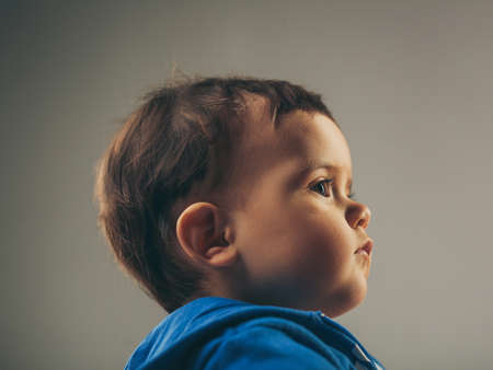 Profile portrait of little child boy with dark hair, serious face expression, wearing casual blue hoodie, isolated in studioの写真素材