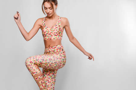 Slim young woman in sport outfit, tight colorful leggings and top with geometrical patterns in a motion, happy, joyful, jumping, isolated in studioの写真素材