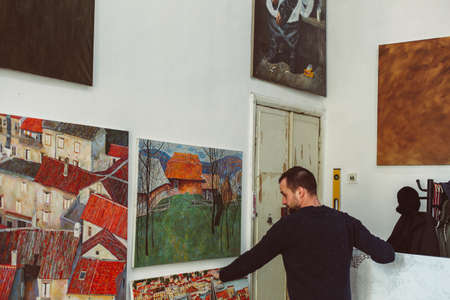male artist is hanging pictures in his art studio, lots of colorful pictures, creative atmosphereの写真素材