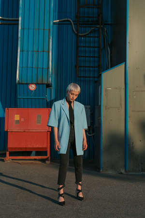 Stylish young eccentric woman with white short hair, wearing blue jacket and black tie, looking...