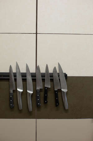 Set of knives hanging on the magnet on the wall in the kitchen