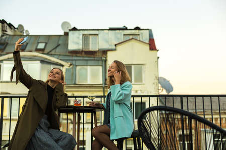 Two friends young beautiful women are sitting in cafe on the terrace on the roof  in old city centre...